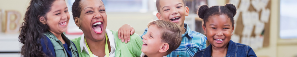 Black teacher laughing with a diverse group of four elementary school students.