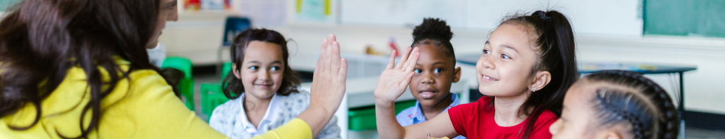 Teacher high-fives smiling elementary student as classmates watch and smile.