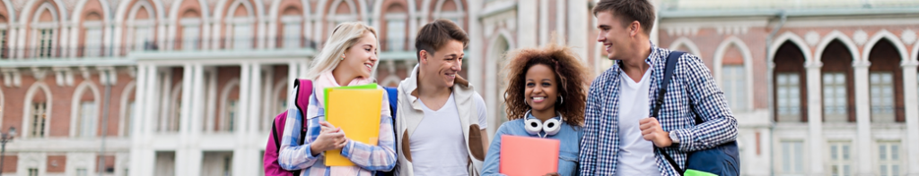 Four diverse high school students smiling and walking side by side as a group with a college building behind them.