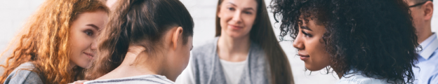 Woman with compassionate expression comforts another woman in a group of several professionals.