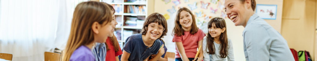 Elementary teacher and students sit in a circle smiling and laughing.