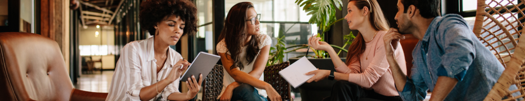 Group of four casual professionals discussing ideas from a paper and tablet two of the individuals are holding.