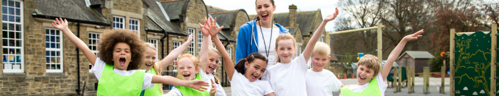 Diverse group of elementary students in matching white tee shirts and their white female teacher stand with their arms outstretched smiling with school pride.