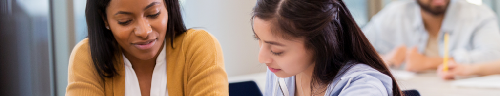 A Black female teacher assists a Latina student.