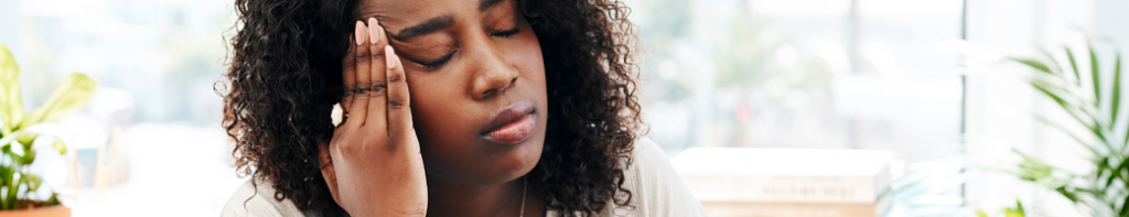 Black woman rests her head in her hand with her eyes closed expressing exhaustion.