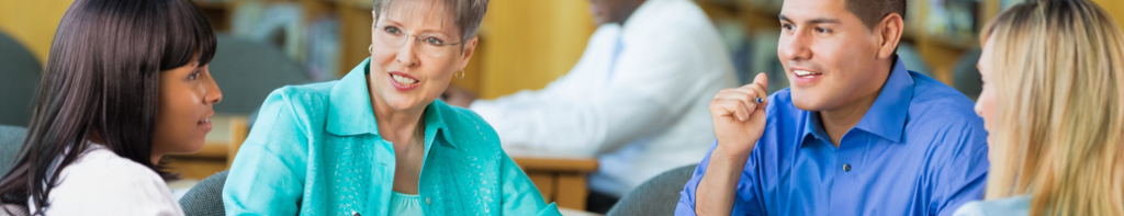 Group of four diverse teachers sit in a circle around a table and discuss ideas.