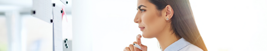 Middle eastern female professional viewed at profile thinking while reviewing documents on a whiteboard.