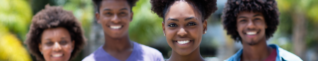 Four smiling Black high school students outside shoulder to shoulder with a female in the center as the main focus.